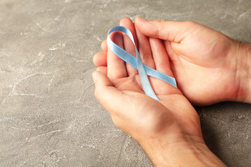 Hand holding blue breast cancer ribbon on grey background. Concept lung cancer awareness.