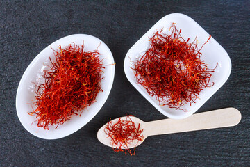 Dry Saffron spice stamens on white plate on a black board. Red threads of saffron.