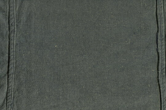 Texture of coarse natural khaki fabric, similar to burlap, with seams at the edges. Background of rough old fabric.