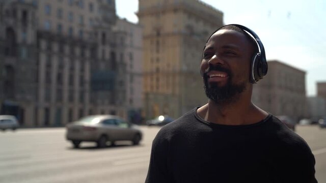 Close-up portrait of a beautiful African-American man with headphones listening to music. City in the background