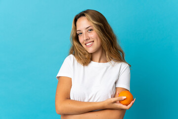 Young blonde woman isolated on blue background holding an orange