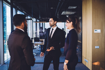 Crew of formally dressed employees collaborating on business project standing in modern office and discussing ideas during CEO conversation, experienced male and female professionals brainstorming