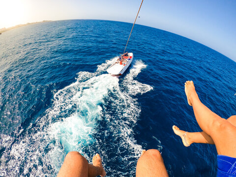 close up and portrait of legs of two people flyig on the air while a boat is pulling them - adults having fun together at summer doing parascending and enjoying their vacations