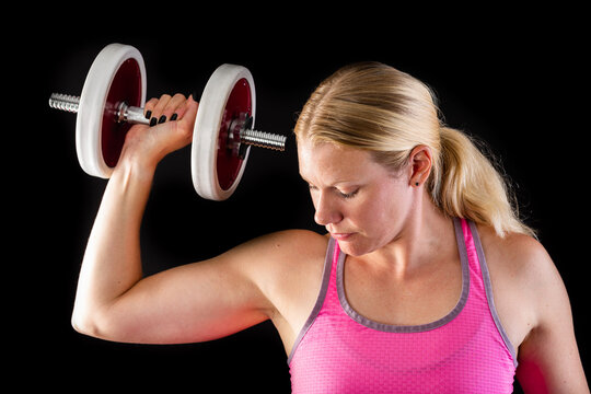 Fitness woman wearing pink top lifting dumbbell isolated on black background