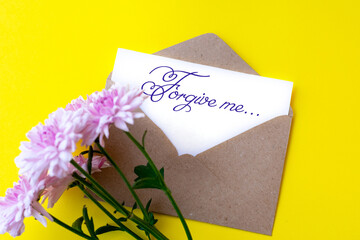 Love envelope and letter with written words forgive me with pink chrysanthemum flowers on bright yellow bacground.