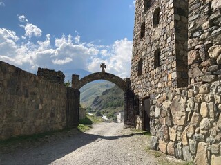 Close up of stone gate with wooden cross on background of mighty mountains and cloudy sky. Entrance to ancient temple on sunny summer day