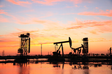 Fototapeta premium in the evening, oil pumps are running, The oil pump and the beautiful sunset reflected in the water, the silhouette of the beam pumping unit in the evening.