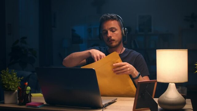 Young man opens letter with documents while working at home at night