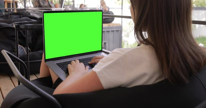 Woman using MacBook Pro laptop with keyed blank green screen in outdoor cafe food market. Travel freelance business lifestyle. Internet communication chat. Typing message, searching. Chromakey mockup