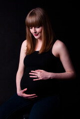Portrait of a thoughtful pregnant woman with a black background, looking away from camera.