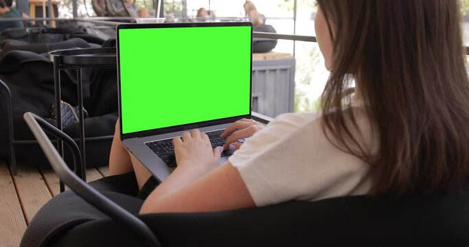 Woman using MacBook Pro with keyed blank green screen in outdoor cafe food market. Travel freelance business lifestyle. Internet communication chat. Typing message, searching. Chromakey mockup