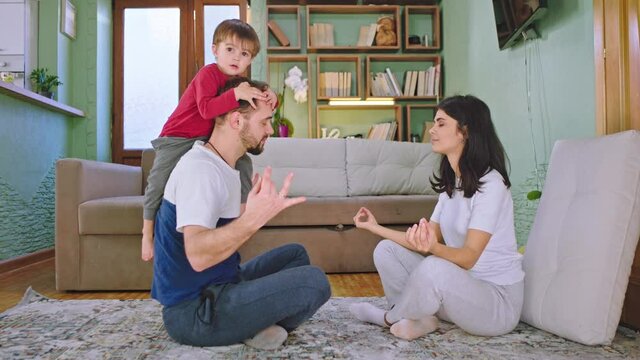 In the living room dad and young mom with their small kid doing yoga together while sitting on the floor they spending time at home
