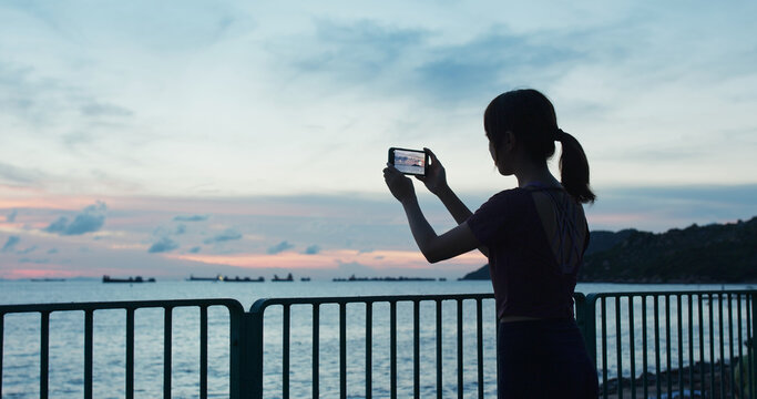 Woman use of mobile photo take photo at sunset time beside the sea