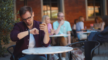 Young handsome man sitting at cafe table waiting for meeting checking time on wristwatch