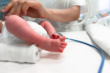 Nurse takes action to monitor and care for premature baby, selective focus - newborn baby foot with a neonatal pulse oximetry monitor and nurse arm. Newborn is placed in the incubator. Neonatal ward