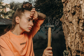 Attractive girl wipes sweat from her forehead and hammers in a nail