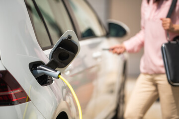 Close up of an electric car charger with a female silhouette locking the car in the background