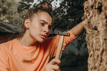 Beautiful girl hammering a nail with a hammer with a focused face