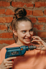 attractive girl with a drill on a brick wall background.