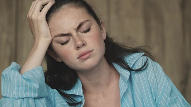 A displeased woman is touching her temples while working with paper documents while sitting at home