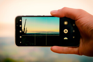Hand holding a smartphone for landscape photography.