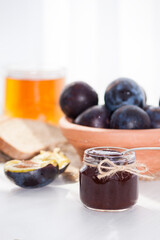 Sweet homemade plum jam and fruits on a white table in a sunny day.
