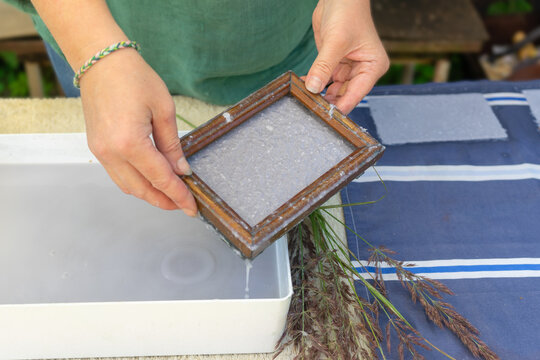 Woman holding frame for making paper sheets from waste paper pulp. Selective focus. Decorative and applied art. Recycling concept, ecology.