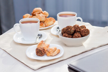 Fresh homemade sugar cookies with tea, grey laptop on white table with sun lights. Work from home concept.