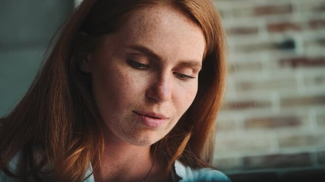Young beautiful redhead woman sitting at the table indoors at home while writing notes
