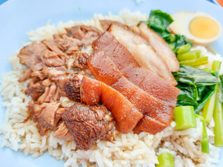 Street food Thai, Braised pork leg rice and half chicken egg, soft-boiled kale topped with rich broth served in a white plate with sour dipping sauce