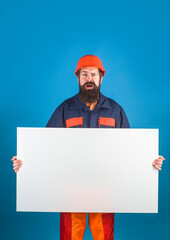 Confused builder holds empty advertising banner. Bearded worker shows empty board. Ready for your text. Man with blank sign board. Space for text.