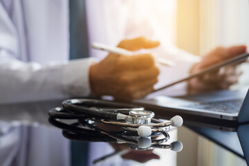 Doctor man in white coat hand using modern digital tablet, work on laptop computer.