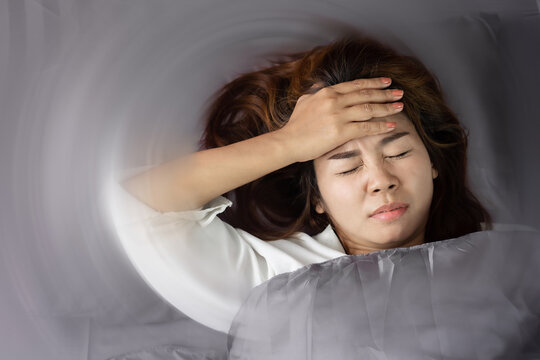 unwell Asian woman having headache , migraine or vertigo  lying in bed with hand holding her head 