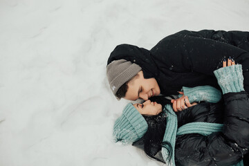 Loving couple hugging in winter forest. Man and woman lying on the snow and having fun. A girl with a guy wallowing in the snow and hugging each other. Valentine's Day. Copy space.