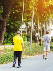 Back view portrait of a Asian elderly man in fitness wear walking and jogging for good health in public park. Senior jogger in nature.  Older Man enjoying Peaceful nature. Healthcare concept.