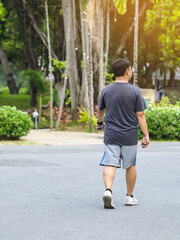 Obraz premium Back view portrait of a Asian man in fitness wear walking and jogging for good health in public park. Jogger in nature. Man enjoying Peaceful nature. Healthcare concept.