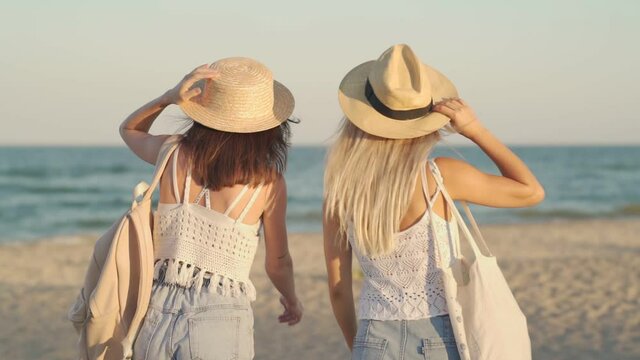 A back view of a smiling girls are walking together on the beach