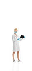 Pointing on tablet. Portrait of female doctor, nurse or cosmetologist in white uniform and blue gloves on white studio background. Copyspace for ad. Concept of healthcare and medicine, beauty, self