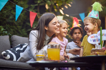  beautiful caucasian female cuddling and smiling with group of children at birthday party