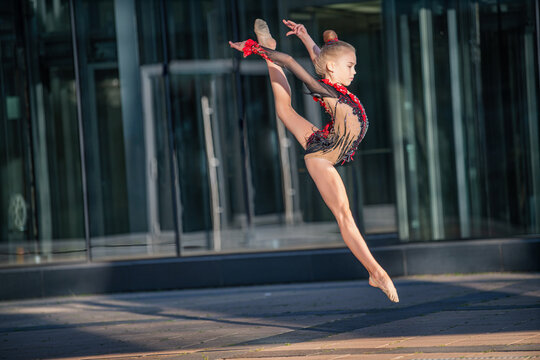 A girl gymnast of school age in a beautiful cross-dress with a black suit performs an exercise without an apparatus.