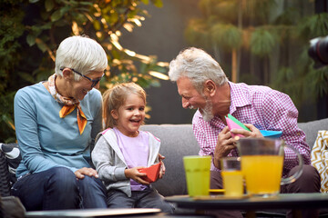 grandparents laughing, enjoying with their granddaughter, sitting outdoor on sofa