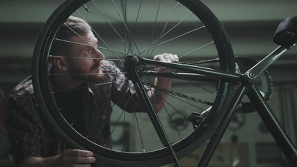 The cyclist repairs the bike in a garage, turns the wheel - Powered by Adobe
