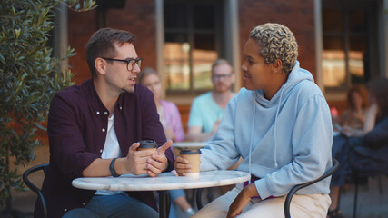 Happy multinational couple talking and smiling while drinking coffee in cafe outdoors