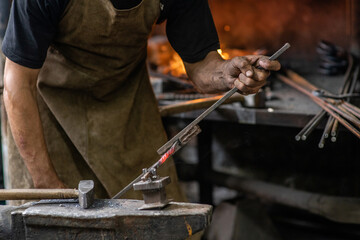 Blacksmith bends iron rod on the anvil with tool