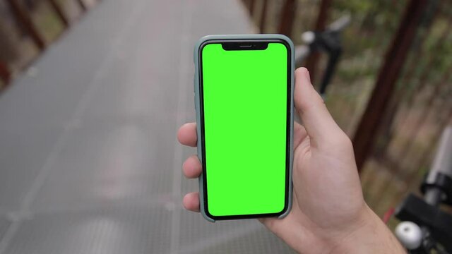 POV Close-up young man watching on iPhone 11 green mock-up blank screen browsing social network in smartphone walking outdoors in the urban park street.