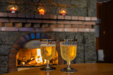 Two plastic glasses with cold champagne on the background of a burning fireplace.