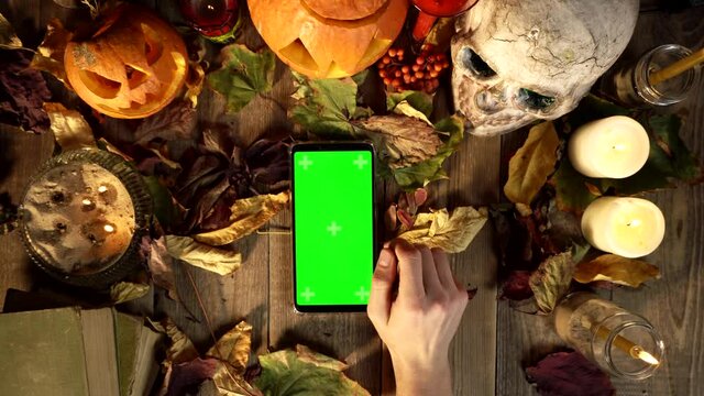 Gestures for using a vertical smartphone on the background of Halloween decorations. Top view objects for all saints day and phone. Mystical tradition in harvest autumn desk decor, copy space template