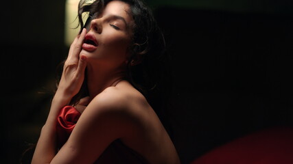 Passionate woman biting lips on bed. Bare girl playing hair in dark bedroom.