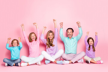Full size photo of delighted big family daddy mommy three small preteen kids celebrate lottery win raise fists sit floor legs crossed folded isolated over pastel color background