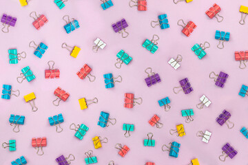 Multi-colored binder clips scattered over a pink background